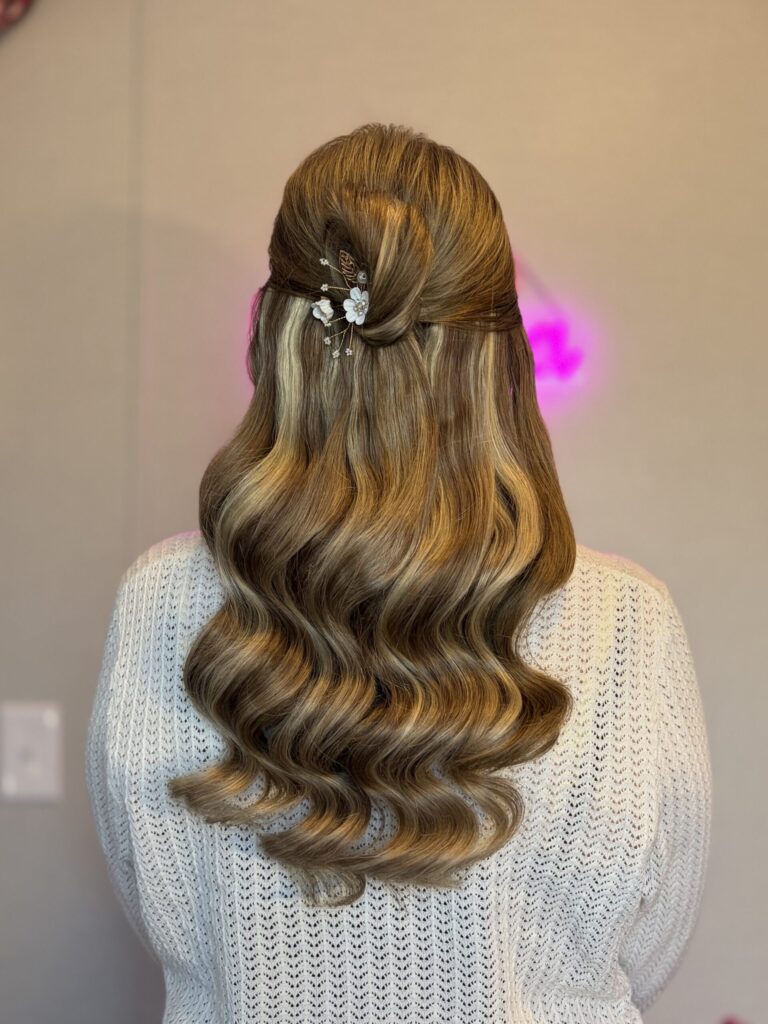 Half-up Half-down bun on light brown hair with honey blonde highlights, loose waves at the bottom. Pinned with an ornamental floral detail on the back. Styled at the Belleza home studio. 