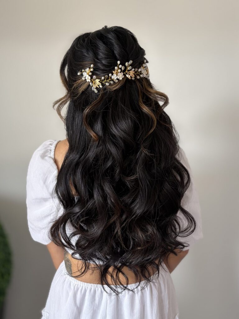 Bridal model from behind with romantic long black curled hair. Hair is in a half-up half-down style held up with a floral champagne gold hair ornament. Hair styled in Ann Arbor by Jaya Ronquillo at the Belleza Bridal Studio.