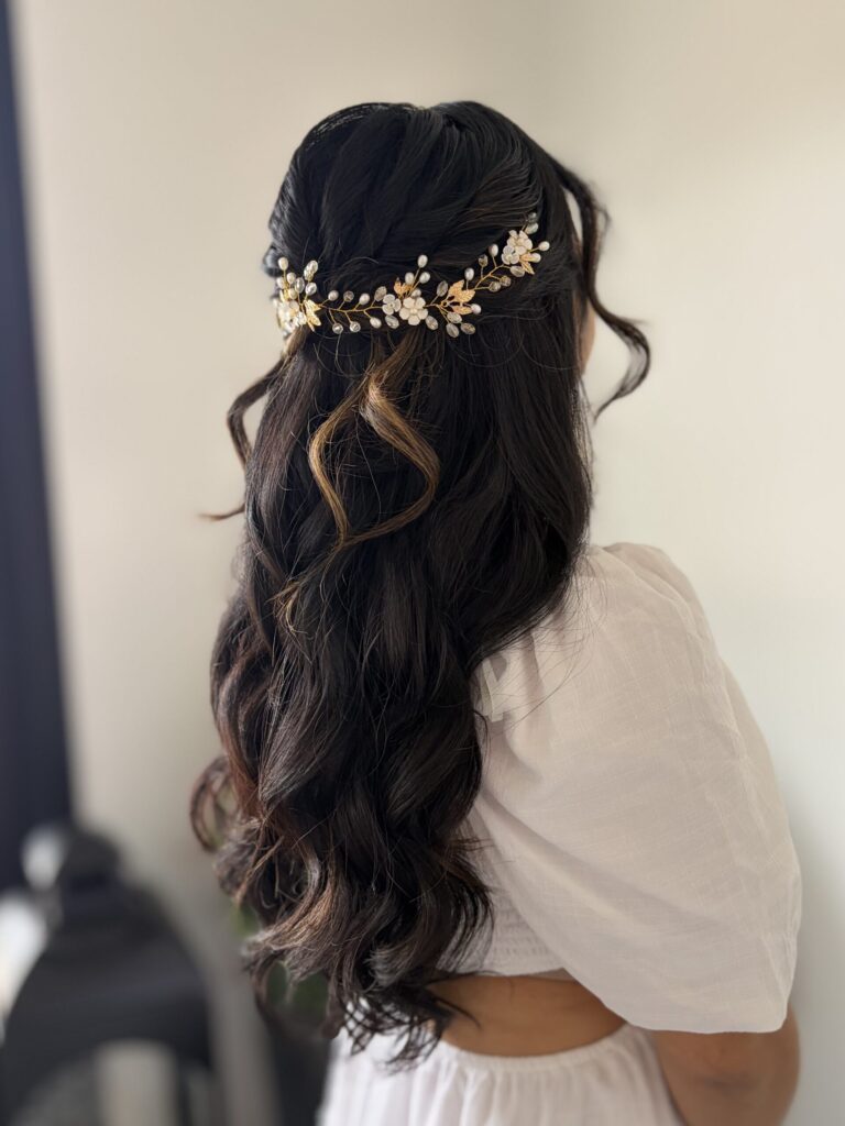 Bridal model from behind with romantic long black curled hair. Hair is in a half-up half-down style held up with a floral champagne gold hair ornament. Hair styled in Ann Arbor by Jaya Ronquillo at the Belleza Bridal Studio.