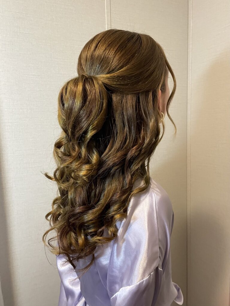 Brunette bridal party memeber with a half-up half-down style featuring loose wavy curls and a twisted feature along the crown, and face framing. Styled by Jaya R at the Belleza home studio. 
