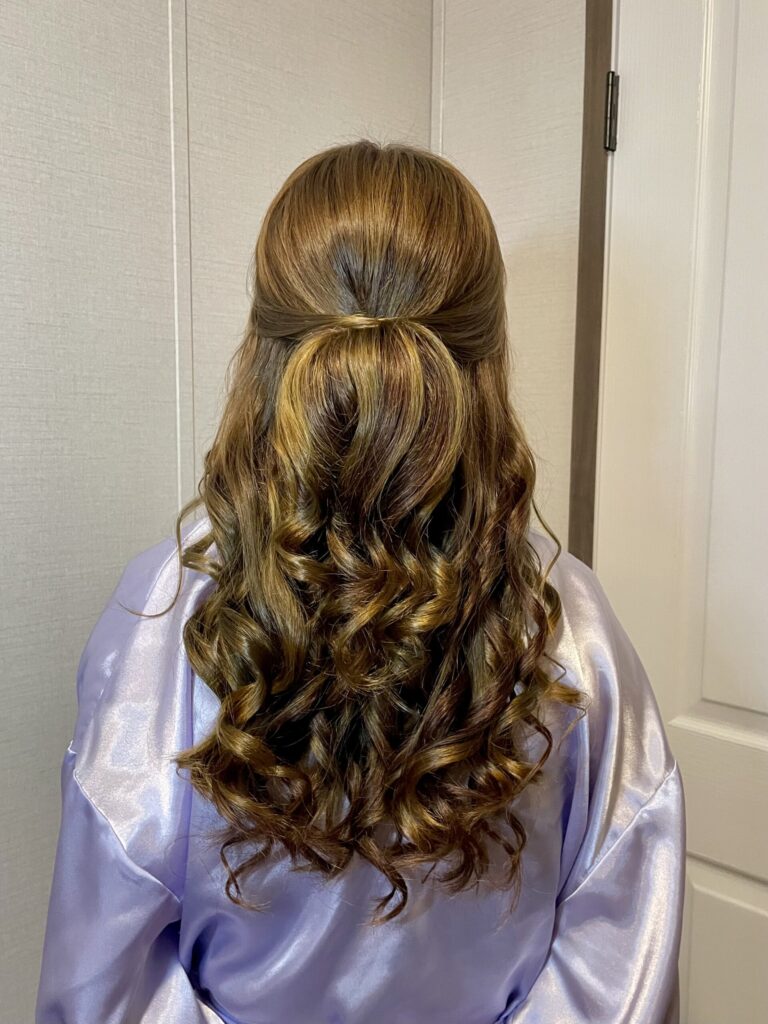 Brunette bridal party memeber with a half-up half-down style featuring loose wavy curls and a twisted feature along the crown, and face framing. Styled by Jaya R at the Belleza home studio. 