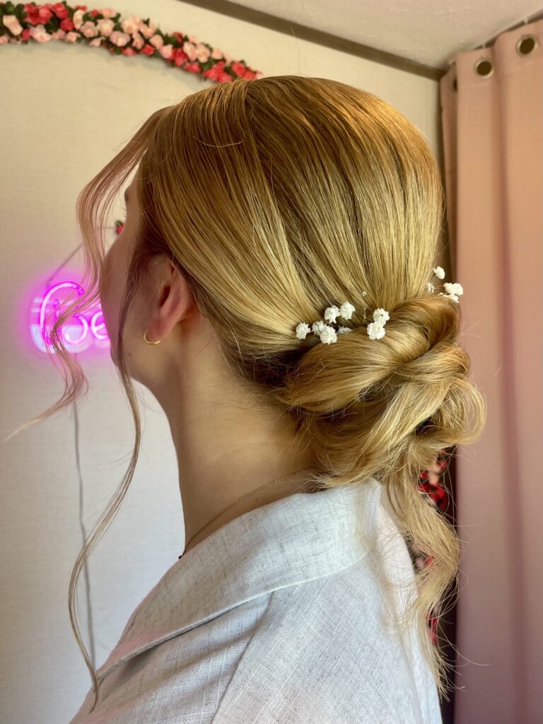 Bridal Model with honey blonde low updo in a bun with flowers and curled face framing.
