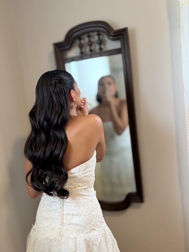 Bride with shiny black Hollywood Waves putting on lipstick in the mirror. 
