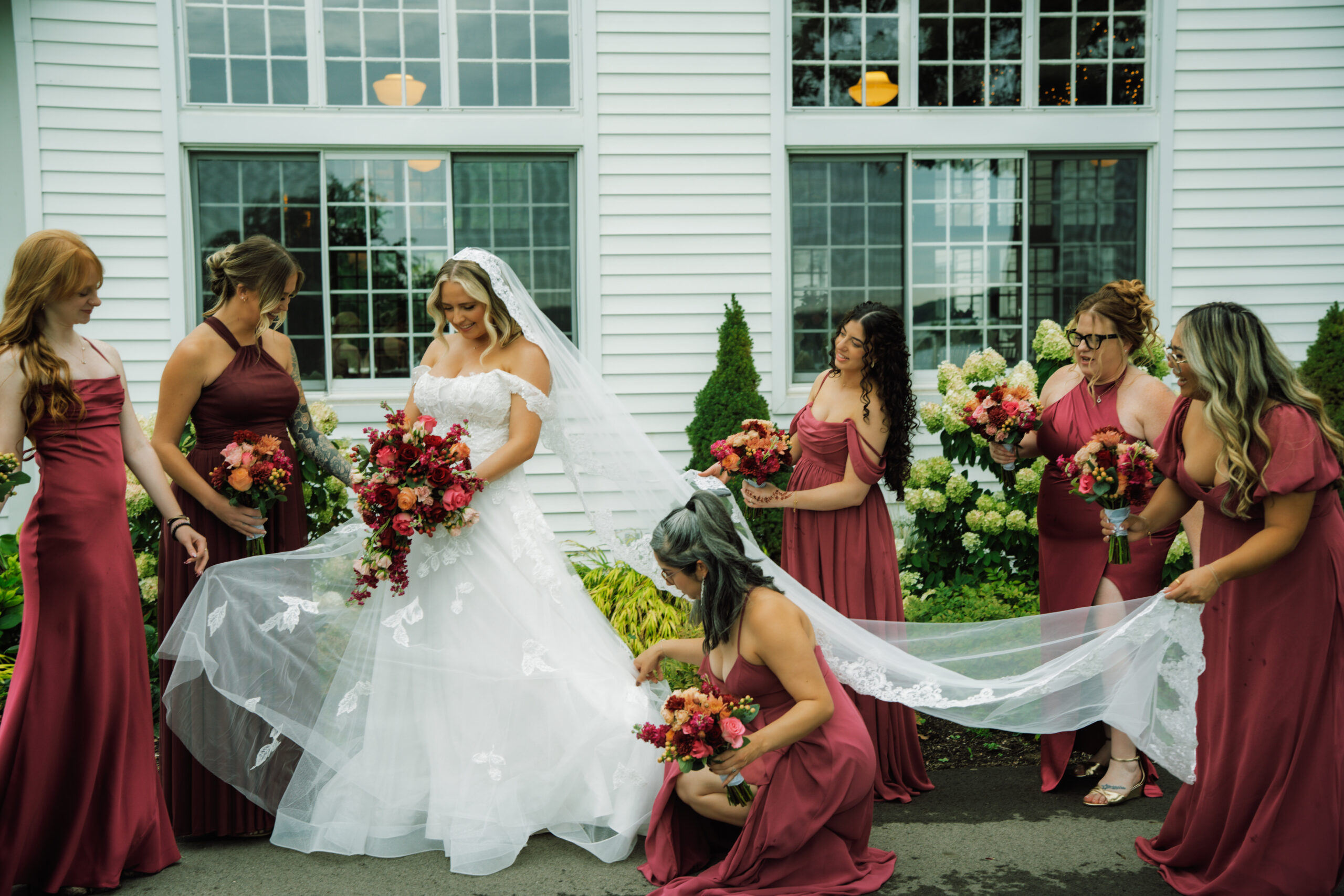 A bride and her bridal party. Bride is holding red flowers and the bridesmaids have matching red dresses.